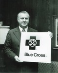 J. W. Herbert posing with a Blue Cross sign